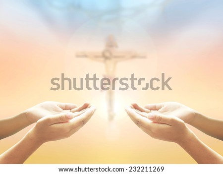 Hands of man praying over blurred crown of thorns and Jesus on the cross over a colorful sunset.