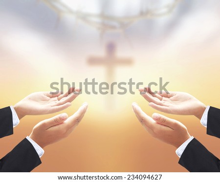Hands of businessman praying over blurred crown of thorns and the cross on a sunset.
