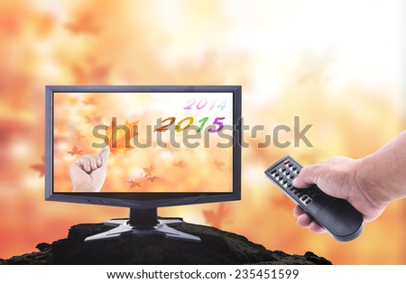 2014-2015 change represents the new year 2015. Human hand holding remote and TV LCD monitor display fruitful text for 2014, 2015 and human hand holding leaf on blurred nature over the actual location.