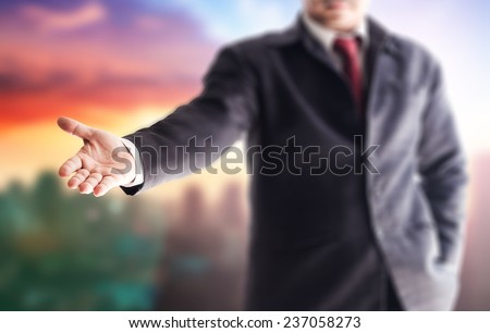 A business man with an open hand ready to seal a deal over blurred city on sunset background.