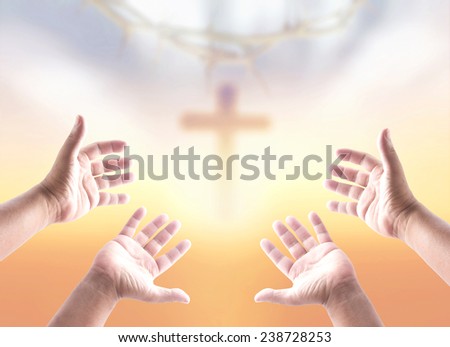 Hands of two men praying over blurred crown of thorns and the cross on a sunset.