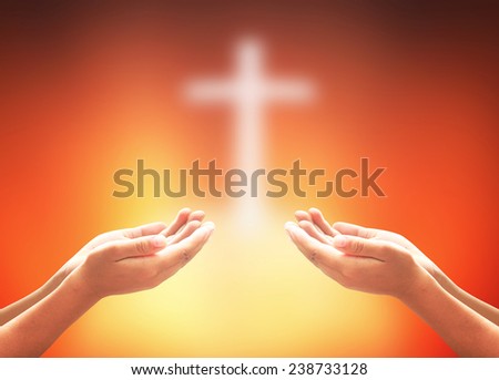 Hands of two men praying over blurred the cross on a sunset.