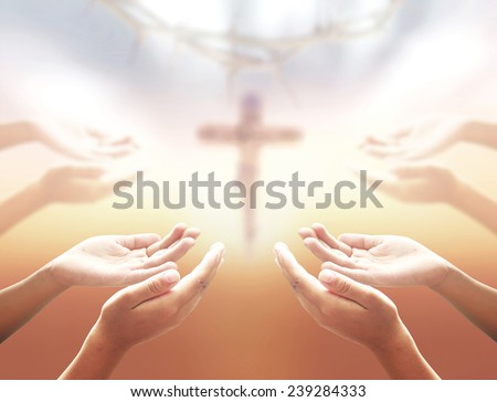 Human hands praying over blurred crown of thorns and Jesus on the cross over a sunset.