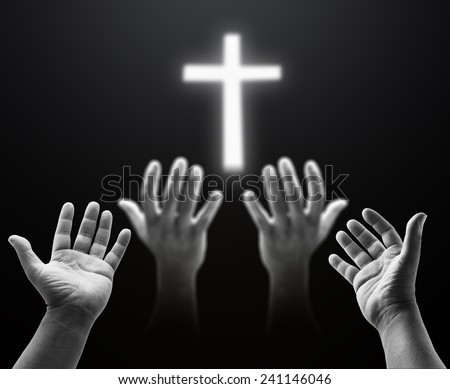 Two people pray together, focus on hands of near and blurred another one, over blurred the white cross.