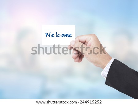 Asian business man holding a handwritten WELCOME over blurred working people in office background.