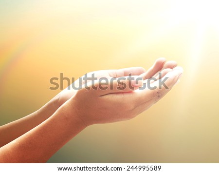 Healing Amazing Light - Human healer with hands open palm up surrounded by a rainbow and ray white light. Praying hand over blurred sunset background.