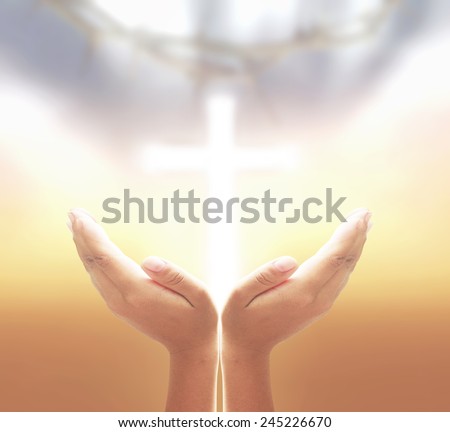 Hands of man praying over blurred crown of thorns and the white cross on a sunset.