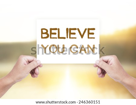Human hand holding a handwritten text for Believe You Can over blurred nature background.
