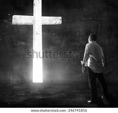 Human standing over the white cross in dark room.