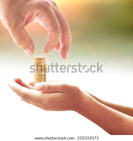 Human hand adding a golden coin in golden coins on another hands over blurred sunset background. Money coin concept.