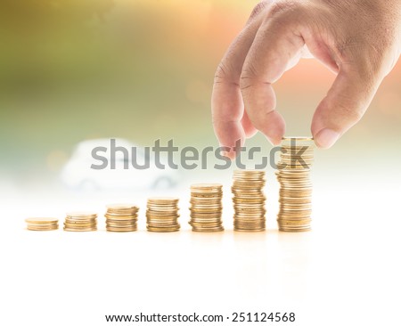Human hand adding golden coin in the final row of gold coins over blurred white car on sunrise, sunset background. Concept for money coin, insurance, buying, renting, repair, fuel , service, holiday.