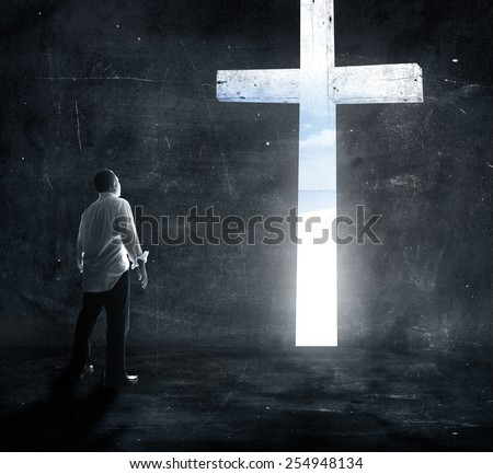 Human standing over the white cross in dark room and looking for freedom.