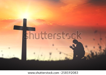 Silhouette human kneeling and praying over the cross on beautiful sunset with amazing light background.