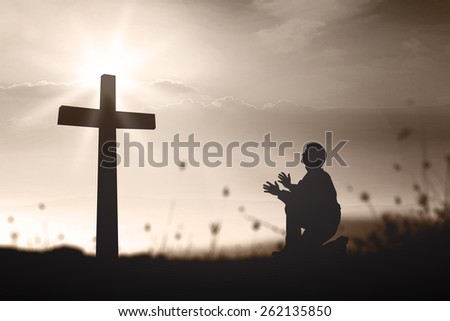 Sepia tone. Silhouette human kneeling and praying over the cross on beautiful sunset with amazing light background.