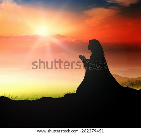 Silhouette of woman kneeling and praying over beautiful sunset background.