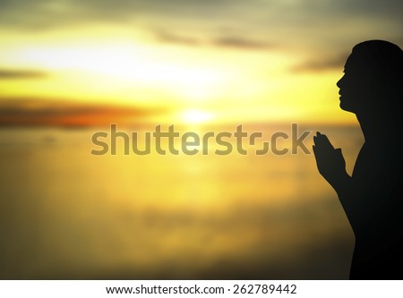 Silhouette of woman praying over beautiful sunset with amazing golden light background.