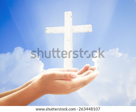 Human hands praying over the white cross and amazing light background.