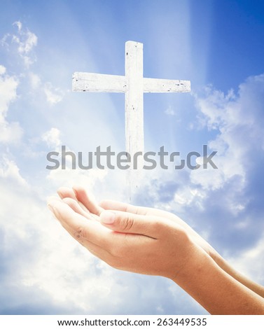 Human hands praying over the white cross and amazing light background.