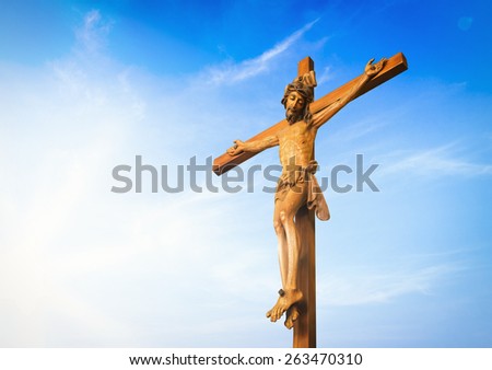 Jesus on the cross over blue sky background. (Public wooden Jesus on the cross)