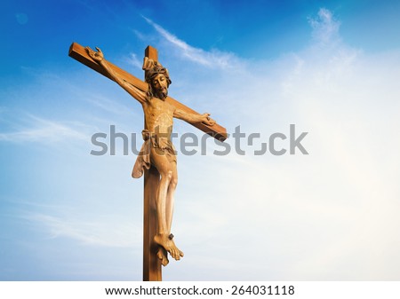 Jesus on the cross over blue sky background. (Public wooden Jesus on the cross)
