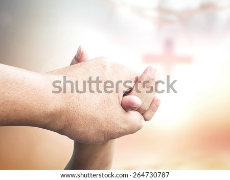 Clasping hand over blurred the cross on sunset background.