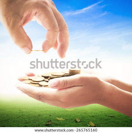 Human hand adding a golden coin into golden coins in another hands on nature background. Money coin concept.