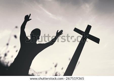 Black and white silhouette human raising hands over the cross on nature background.