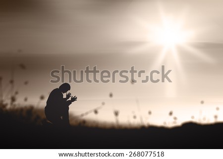 Sepia tone. The lonely man. People kneeling and praying over blurred the white cross on sunset background.
