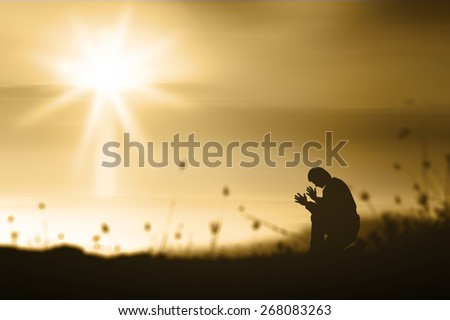 The lonely man. People kneeling and praying over blurred the white cross on golden light sunset background.
