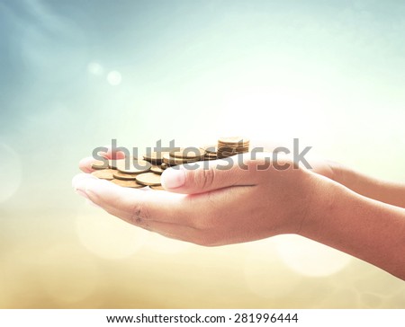 A handful of golden coins in the palm of a hand over blurred beautiful sunset background. Money coin concept.
