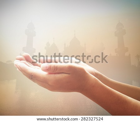 Human open empty hands with palms up over blurred public mosque on sunset background.