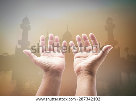 Human open empty hands with palms up over blurred public mosque on sunset background.
