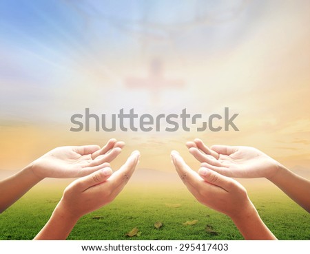 Hands of man praying over blurred crown of thorns and the cross on a sunset background.