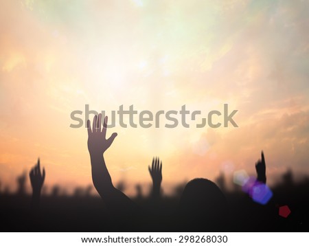 Silhouette people raising hands over blurred the cross on beautiful golden autumn sunset background.