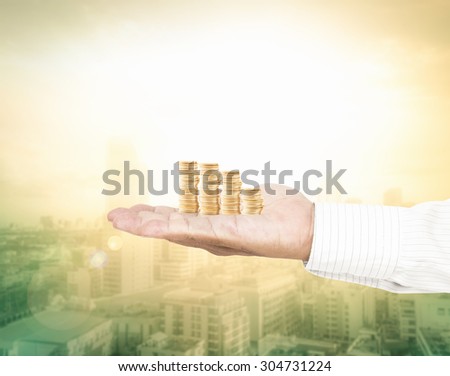 A handful of golden coins in the palm of a hand over blurred sunrise on city with circle light. Investment concept.