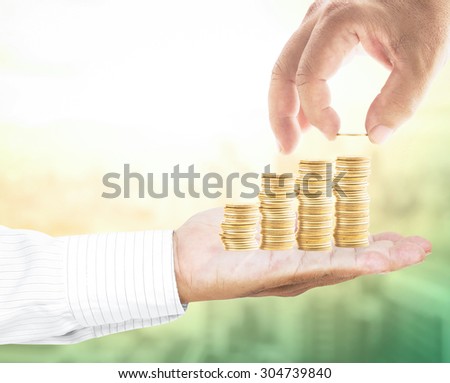 Human hand adding a golden coin in golden coins on another hands over blurred sunrise on city with circle light. Investment concept. Concept for money coin, insurance, buying, renting, Investment.