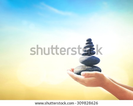 Human hands holding balanced seven Zen stones over blurred beautiful nature background. Ecology, Sustainability concept.