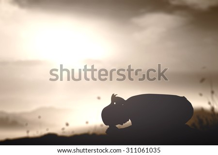 Sepia tone. Silhouette of woman kneeling and praying over beautiful sunset background.