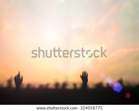 Blurred people raising hands over blurred the cross on beautiful nature background.