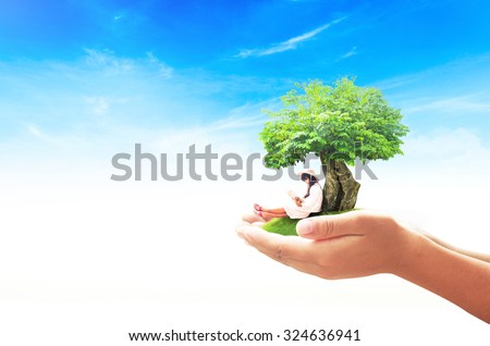 Human hand holding a beautiful asian girl reading a book under big tree on green meadow over blue sky background. World Mental Health Day concept. International Day of the Girl Child concept.