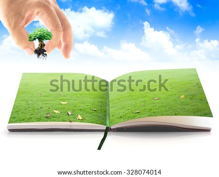 Human hand add growing tree or big plant into opening book in green meadow over beautiful blue sky background. Natural energy concept. Ecology, World Environment Day concept.
