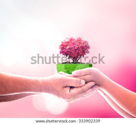 Father and son hands holding growing red big tree in shape heart with a green earth globe of grass on blurred abstract beautiful pink bokeh colorful autumn sunset background. Valentines Day concept.