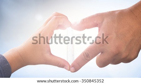 Father and son hands up to blue sky in the shape of a heart with the white cross around the sun. Fathers Day, Creation, Love, Valentines Day, God and Adam, Holy Bible, Health Care concept.