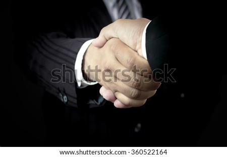 Closeup of a businessman handshake in dark room background. Lit, Business, Greeting, Handshake, International Human Solidarity Day, Trust, Respect, Investment, Insurance Agent, CSR, Partner Concept.