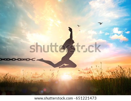 Freedom and independence concept: Silhouette of a girl jumping and broken chains at sunset meadow with her hands raised.