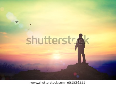 Worshipping concept: Silhouette of humble human standing to worship God in mountain sunset background.