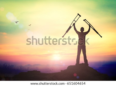 Rehabilitation concept: Silhouette a disabled man standing up and raising his crutches at mountain sunset background.