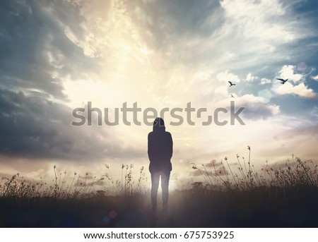 Faith and question concept: Silhouette alone woman standing on meadow sunset background.