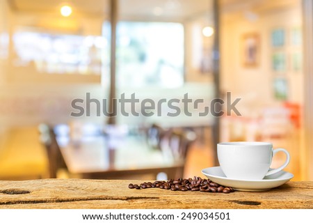image of white cup of coffee on wooden board with Coffee shop blur background with bokeh.