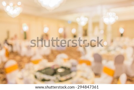 blurred image of Large dining table set for wedding, dinner or festival event with beautiful lights decoration inside large hall with people.